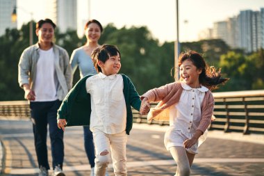 happy asian family with two children walking on pedestrian bridge in city park clipart