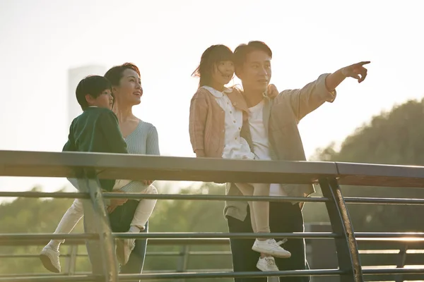 亚洲家庭 有两个孩子站在人行天桥上 黄昏时分观望城市公园的景色 — 图库照片