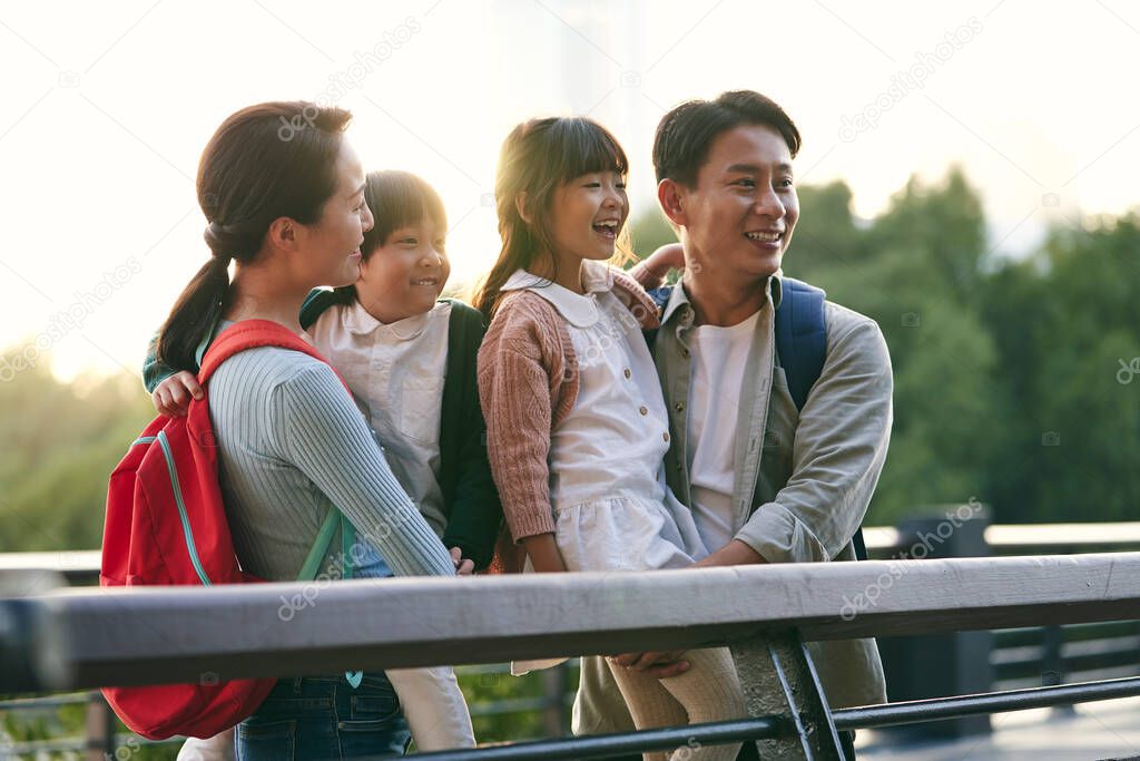 asian family with two children standing on pedestrian bridge looking at view in city park