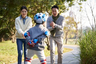 Asyalı ebeveynler oğlana şehir parkında paten kaymayı öğretiyor.