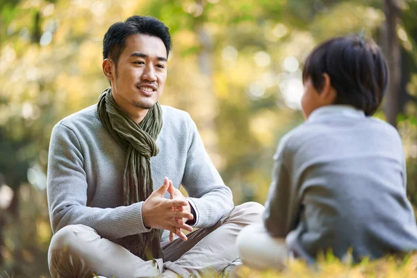 Asian Father Son Sitting Grass Having Pleasant Conversation Outdoors Park — Stock Photo, Image