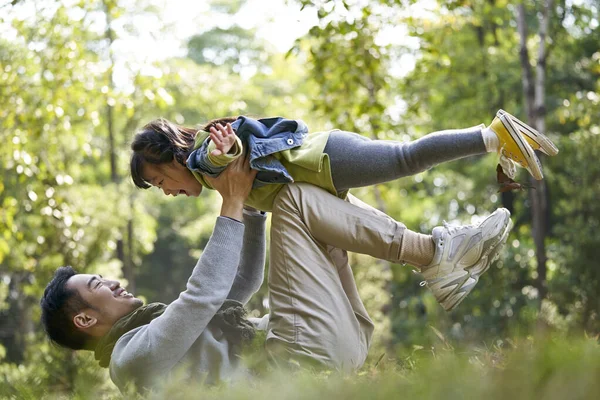 Азиатский Отец Лежит Траве Хорошо Проводит Время Поднимая Дочь Воздухе — стоковое фото