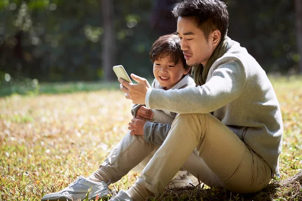 Joven Asiático Padre Leyendo Historia Hijo Usando Celular Aire Libre — Foto de Stock