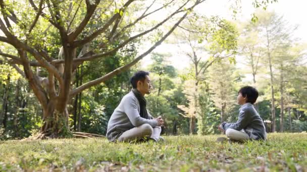 Ασιάτης Πατέρας Και Γιος Κάθονται Στο Γρασίδι Στο Πάρκο Και — Αρχείο Βίντεο