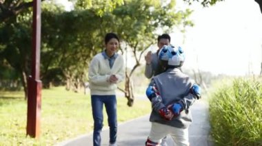 Küçük Asyalı çocuk paten öğreniyor. Ebeveynler teşvik ediyor. 