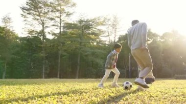 Asyalı baba oğluyla parkta futbol oynuyor.