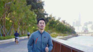 Genç Asyalı adam nehir kenarındaki şehir parkında egzersiz yapıyor.