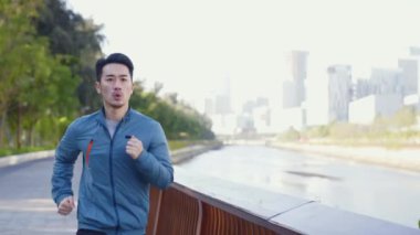 Genç Asyalı adam nehir kenarındaki şehir parkında egzersiz yapıyor.