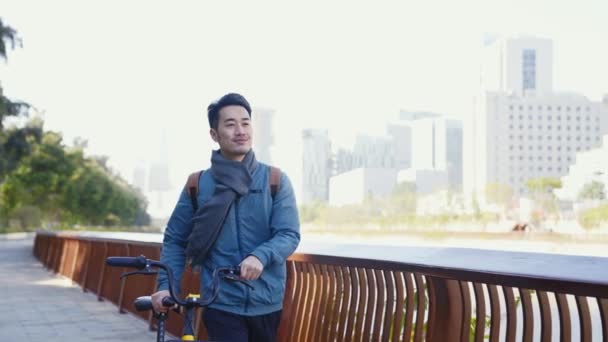 都会の公園を自転車で歩いている若いアジア人男性は — ストック動画