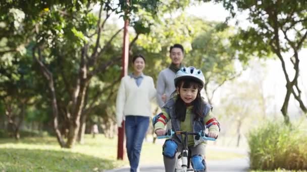 亚洲小女孩骑自行车在公园里 父母在后面看着她 — 图库视频影像