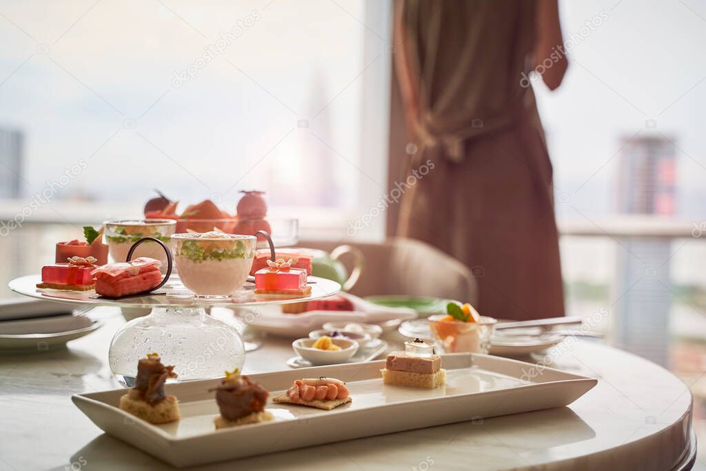 mature asian woman standing by the window looking at city view with food on table in a hotel room