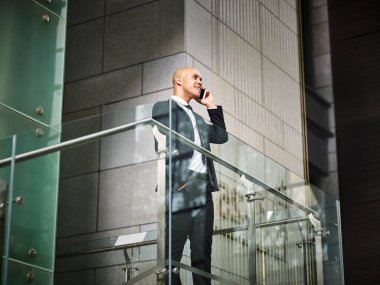 Genç Latin iş adamı merdivenlerin tepesinde duruyor ve modern ofis binasında cep telefonuyla arama yapıyor.