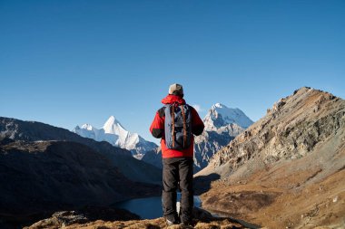 Asyalı erkek sırt çantalı gezgin Yading Ulusal Parkı, Daocheng İlçesi, Sichuan Bölgesi, Çin 'deki dağlara bakıyor.
