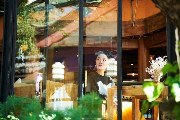 コーヒーショップや茶店に座って窓ガラス越しに見ているアジアの女性 — ストック写真