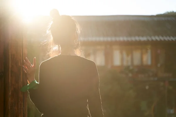 rear view of an asian woman standing in sunlight looking at view