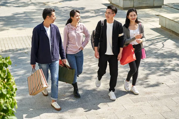 high angle view of group of four young asian people chatting talking conversing while walking on street with shopping bags in hands