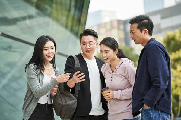 屋外で幸せと笑顔で携帯電話を見ている若いアジア人のグループは — ストック写真