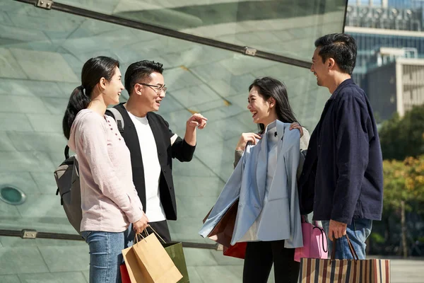 group of four young asian people standing on street talking chatting conversing during shopping trip happy and smiling