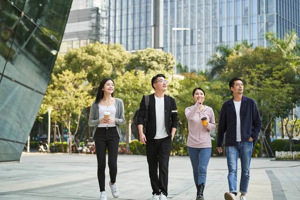 group of four young asian people talking chatting while walking on street in modern city happy and smiling