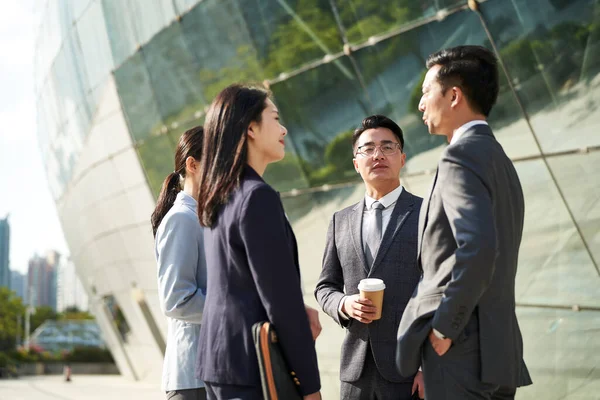 group of four young asian business people standing chatting outdoors on street