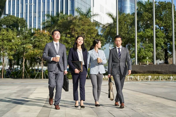 group of four young asian business people walking outdoors on street in modern city