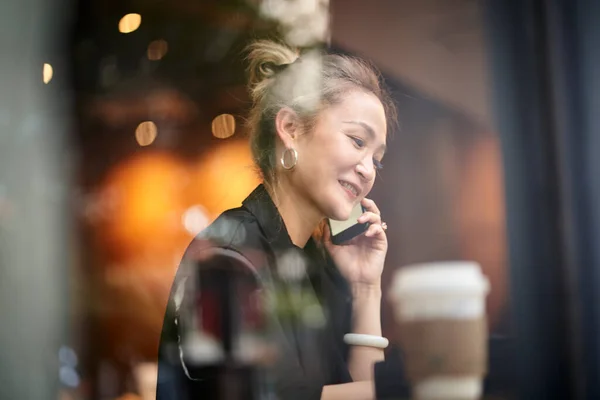 asian woman talking chatting conversing using cellphone in coffee shop