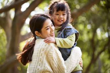loving asian mother hugging cute daughter outdoors in park happy and smiling