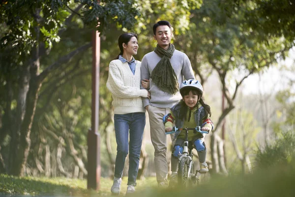 Young Asian Couple Taking Walk Outdoors Park While Daughter Riding — Zdjęcie stockowe