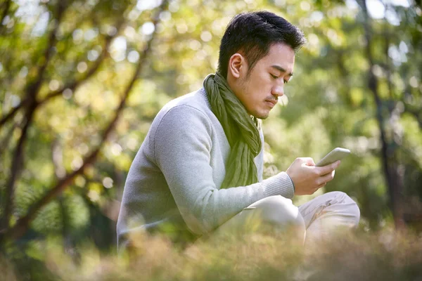 Young Asian Adult Man Sitting Grass Outdoors Park Reading Contents —  Fotos de Stock