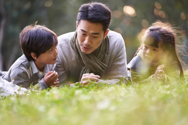 Asiatisk Far Liggande Framsidan Gräs Berättar Historia För Två Barn — Stockfoto