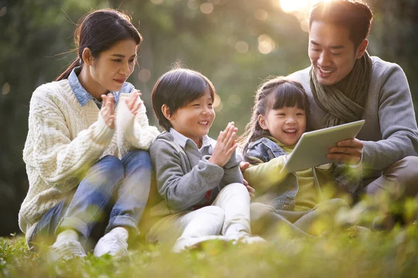 Young Asian Family Two Children Sitting Grass Outdoors Park Watching Foto Stock