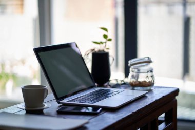 workspace of a freelancer working from home with laptop and cellphone on end table