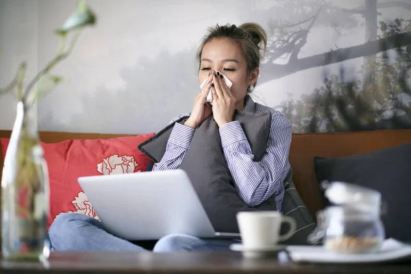 成熟的亚洲女人感冒了 流鼻涕 坐在沙发上用笔记本电脑干活 — 图库照片