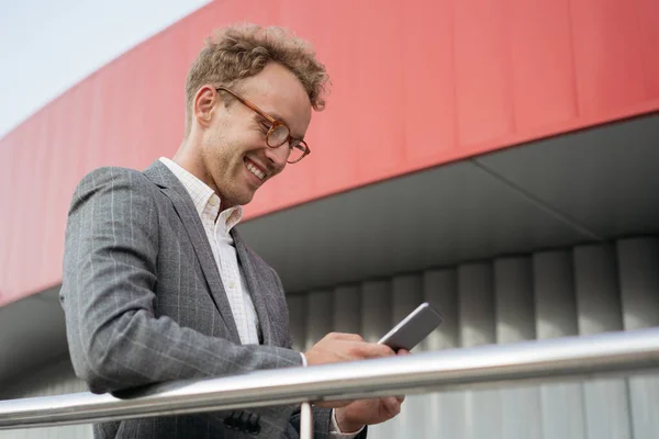 Handsome smiling man holding  mobile phone text messaging, community online, reading news walking on urban street. Confident man using mobile application for online shopping outdoors