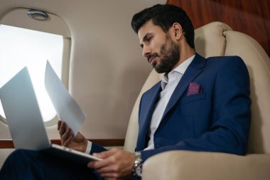 Laptop kullanan yakışıklı, düşünceli orta doğulu iş adamı. Uçakta oturmuş mali raporları okuyor. Zengin, kendine güvenen girişimci. Lüks özel jet, başarılı iş konsepti.