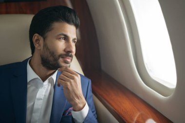 Yakışıklı dalgın Arap işadamı planlama projesinin yakın plan portresi pencerede oturuyor. Zengin, kendine güvenen girişimci. Lüks özel jet, başarılı iş konsepti.