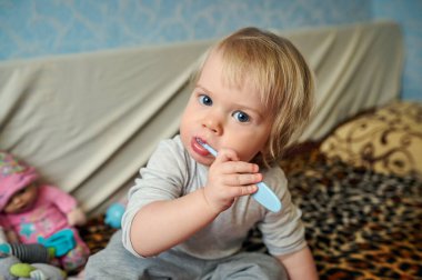 Küçük bir kız kanepeye oturur ve dişlerini fırçalar, kameraya bakar. ev mobilyaları.