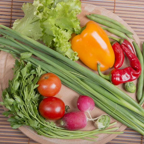 Fresh vegetables on a round board and bamboo mat — Stock Photo, Image