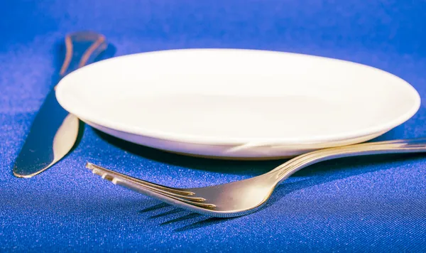 Cuchillo, tenedor y plato sobre fondo azul —  Fotos de Stock
