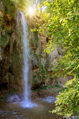 Beautiful waterfall on the mountain with blue sky shining sun. Waterfall in the mountains of the North Caucasus. Nature abstract background.