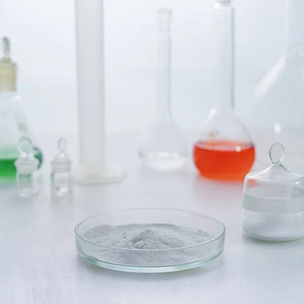 Petri dish with white chemical powder standing on laboratory table next to flasks isolated on white — Foto Stock