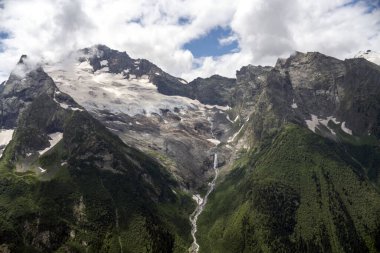 Glacier turning into the river. Mountains in the clouds. Beautiful snow-capped mountains in summer.