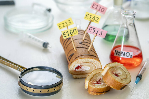 Food additives: sweet roll with chemical additives with colored labels, on a laboratory table. Close up.