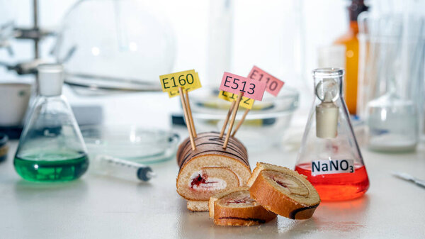 Food additives: sweet roll with chemical additives with colored labels, on a laboratory table.