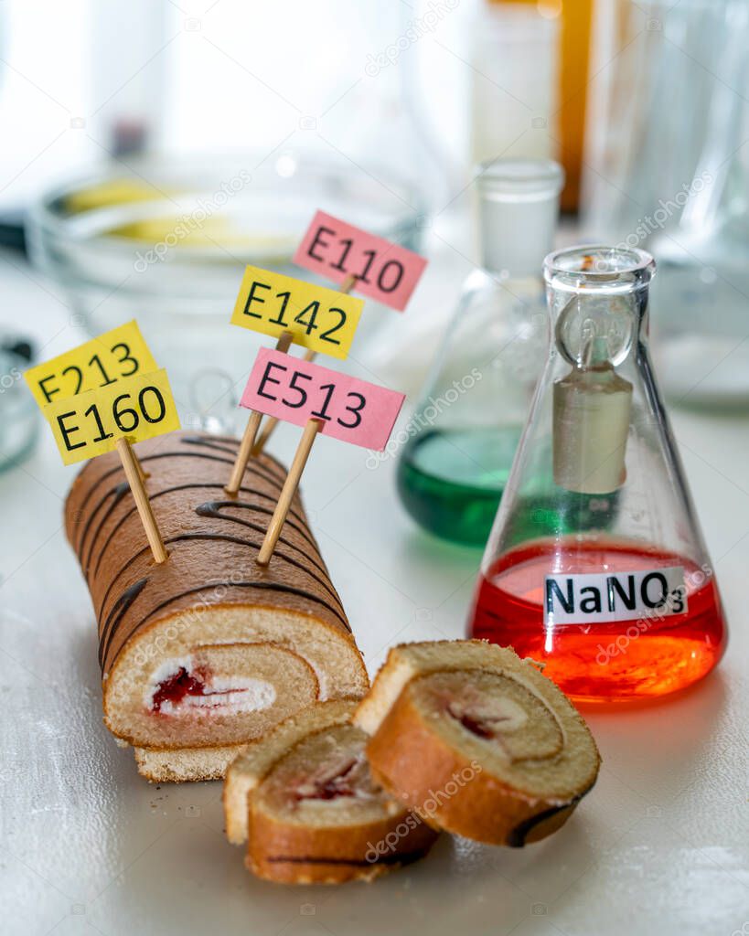 Food additives: sweet roll with chemical additives with colored labels, on a laboratory table.