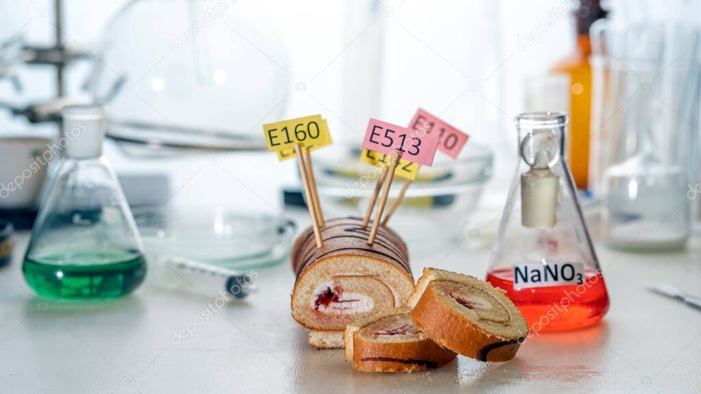 Food additives: sweet roll with chemical additives with colored labels, on a laboratory table.