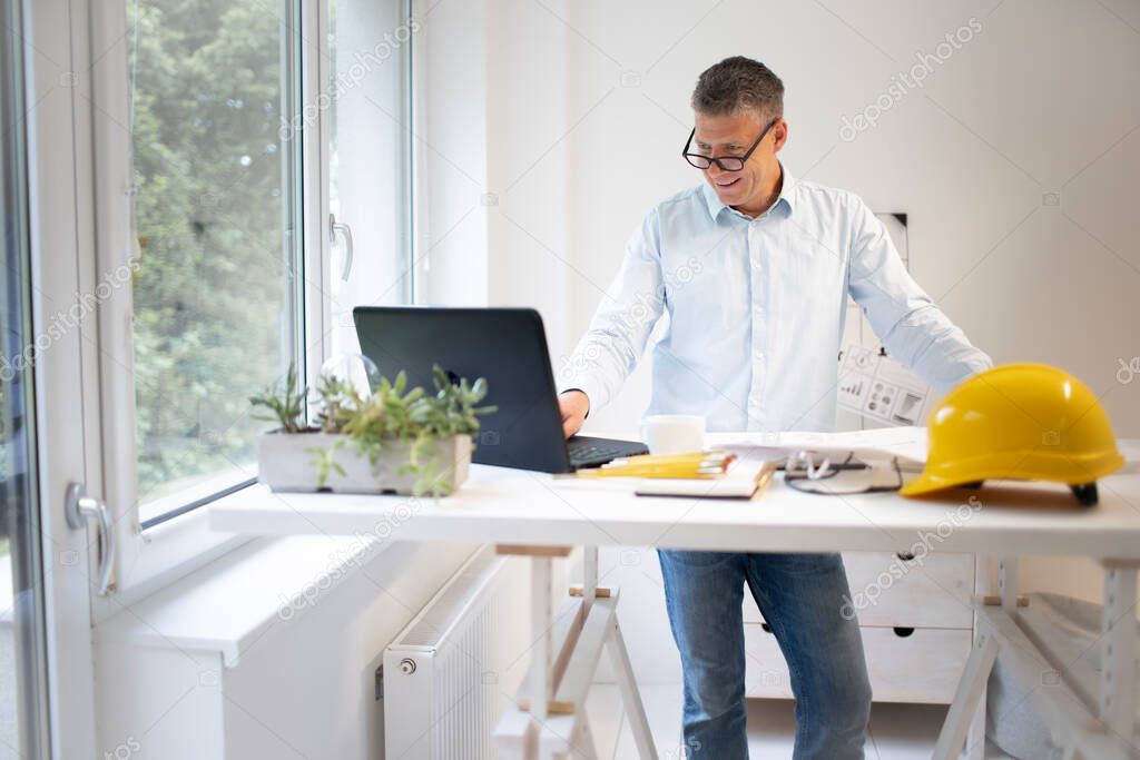 Architect in blue shirt is standing at height adjustable work table and is working