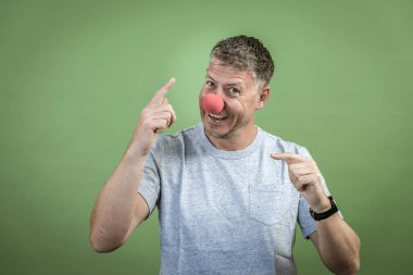 Kırmızı palyaço burunlu ve yeşil arka planda gri gömlekli adam.