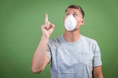 Fffp2 burunlu ve ağız maskeli adam yeşil arka planın önünde duruyor.