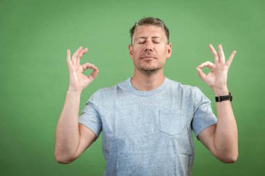 Gri tişörtlü, gri saçlı orta yaşlı bir adam yeşil arka planda poz veriyor.